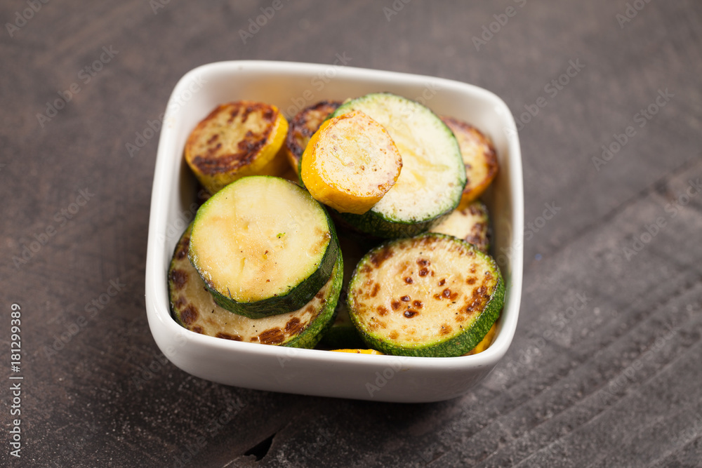 Small white bowl of roasted squash and zucchini on dark background slightly above shot
Small white bowl of roasted squash and zucchini on dark background slightly above shot