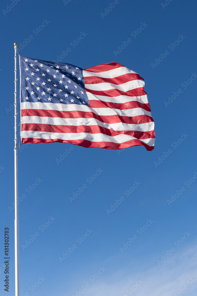The stars and stripes of the American flag against a deep blue sky. Wind is unfurling the flag.