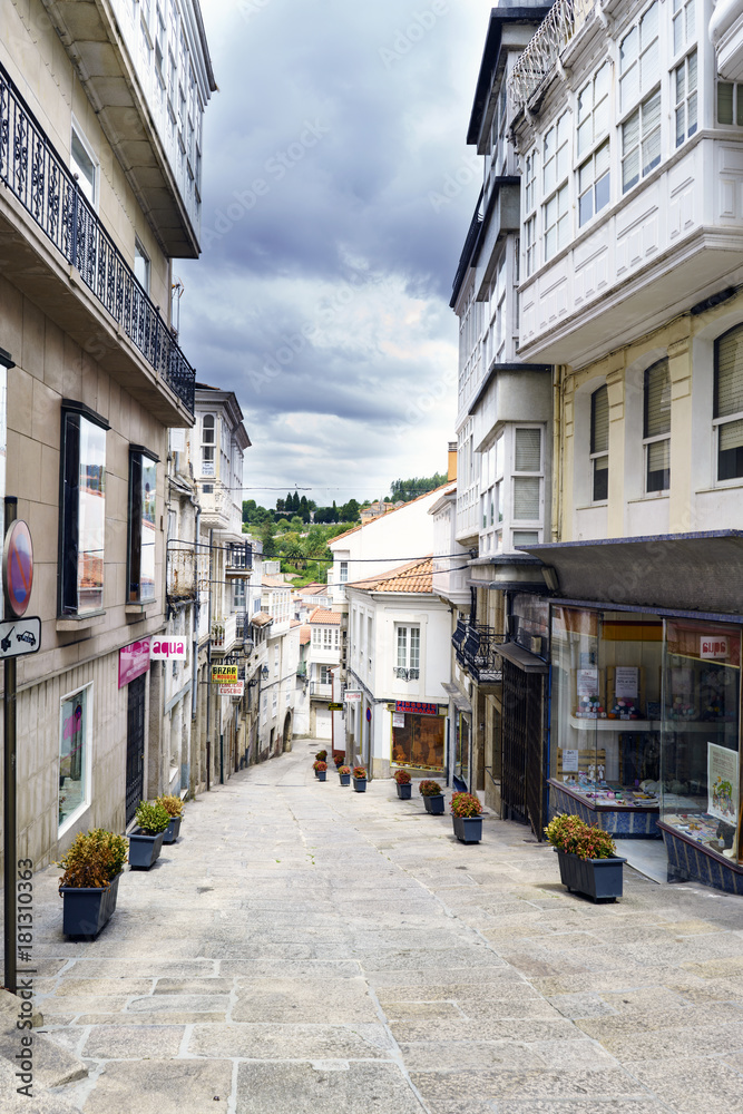 Betanzos, Galicia, Spain. July 30th, 2017: Commercial street with the floor of stone slabs and decorated with flower pots. Sky with clouds threatening rain and without people