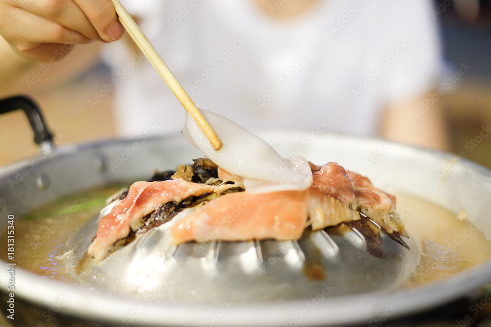 Hand holding chopsticks with squid for grilled on metal stove with pork, beef or chicken and soup - food for winter concept.