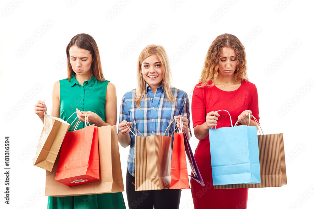 Portrait of three young girlfriends holding bunches of multi-colored shopping bags