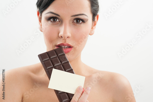 beautiful caucasian model holding a tablet of dark chocolate near her mouth and a business white card on a white background