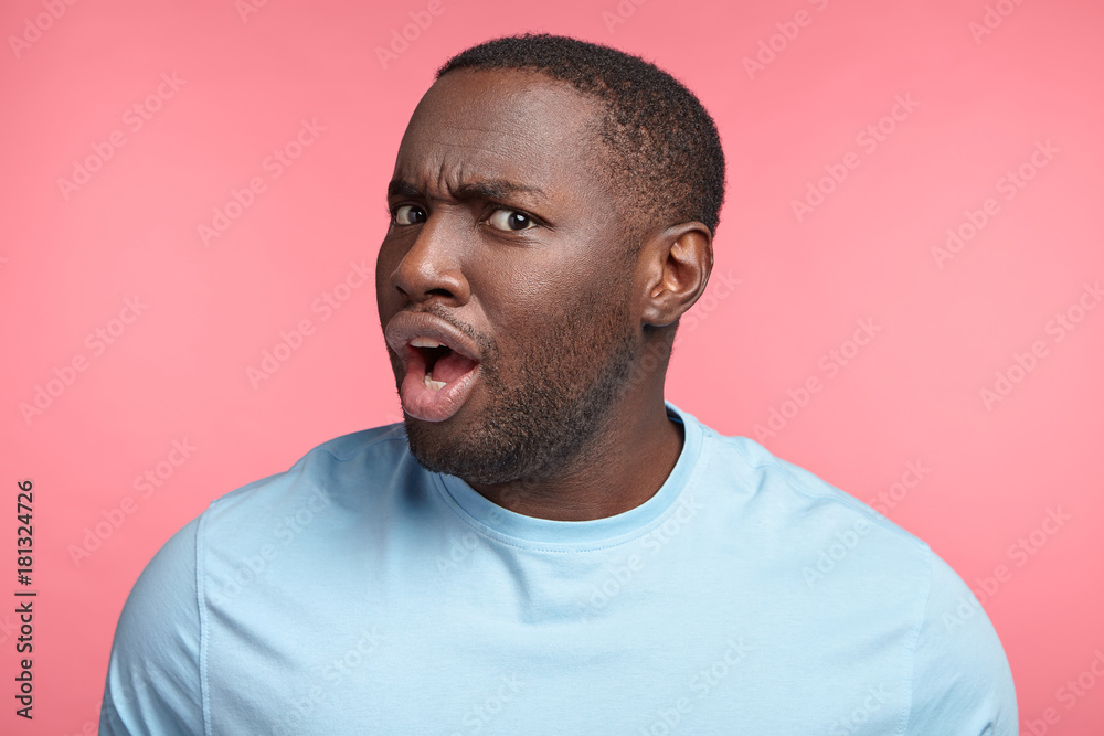 Portrait of indignant outraged black man expresses perplexity, frowns face with dissatisfaction, upset not to be chosen in football team, can`t understand something. People and body language concept