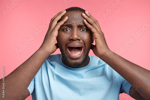 Horizontal portrait of stressful black man screams in panic, has many problems connected with health, sees no way out. Crazy mad troublesome African American male hears shocking news about friend