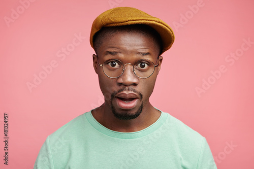 Headshot of emotional excited black man stares at camera with disbelief, can`t undertand or belief in his big failure at international competition, amazed with cool news, says omg poses over pink wall
