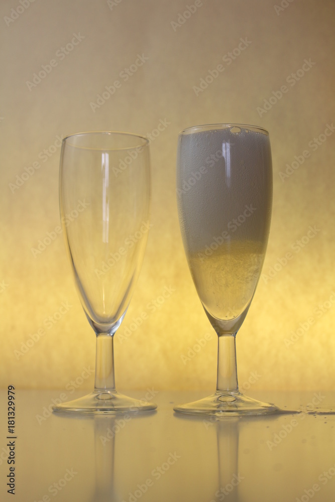 one empty glass of wine, another full of champagne on yellow background