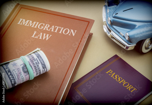 Immigration law book next to a passport and blue miniature vehicle, conceptual image