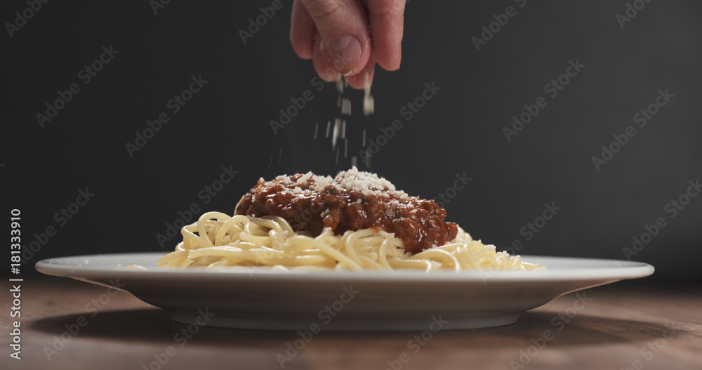man hand sprinkle grated aged parmesan cheese over spaghetti bolognese  Stock-Foto | Adobe Stock