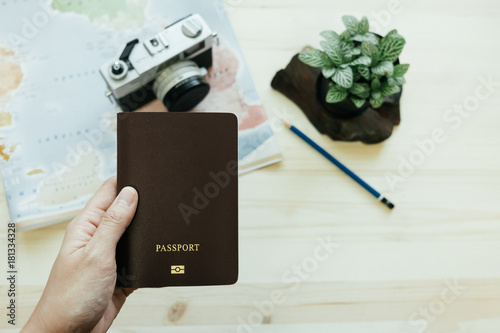 hand of women hold passport has retro camera, world map, pencil, plants placed on wooden table are background. image for equipment, travel, object, gedget, lifestyle, body concept
