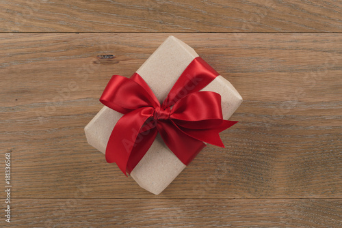 brown paper gift box with red ribbon bow on oak table
