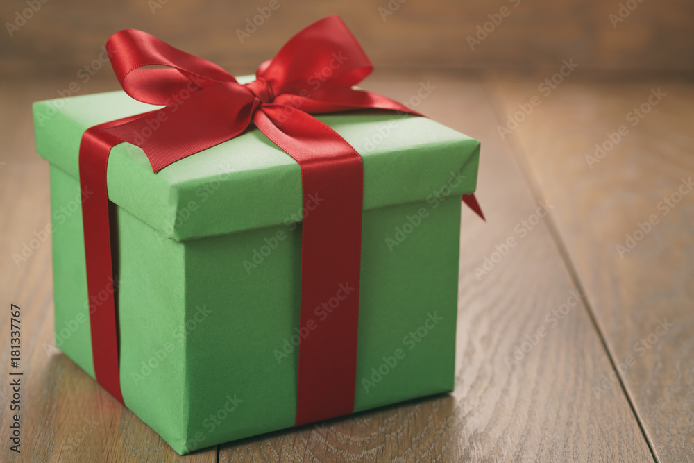 green paper gift box with red ribbon bow on oak table green paper gift box with red ribbon bow on oak table