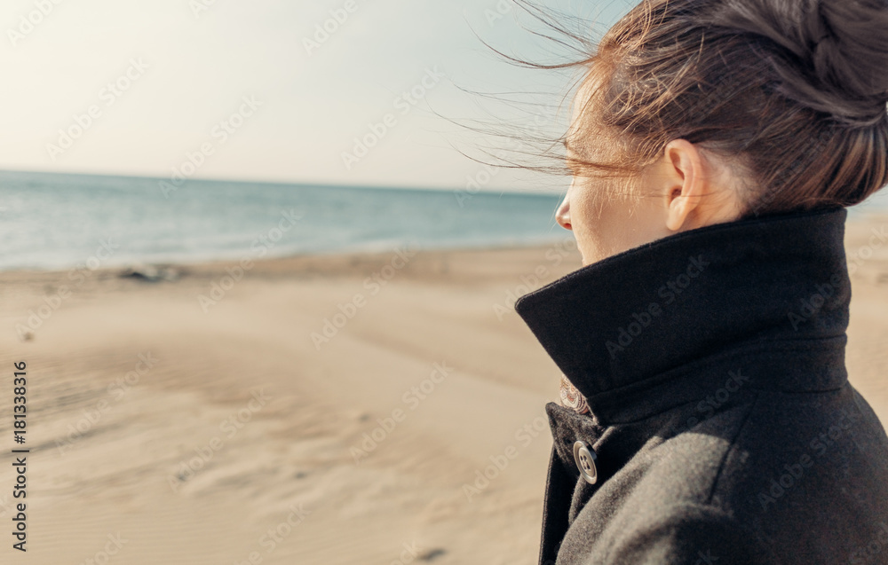 Woman in coat walking on shore.