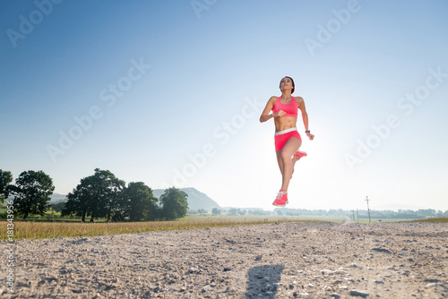 amazing female athlete model wearing pink clothes jumping in the middle of a running workout early in the morning