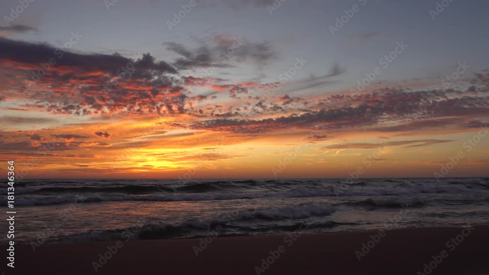 Waves washing ashore with sunset over lake - beautiful clouds in the sky and reflection of sunset on water