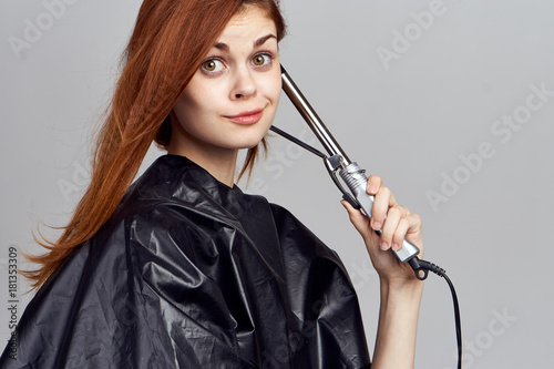 red haired girl hairdresser in black straightens her hair