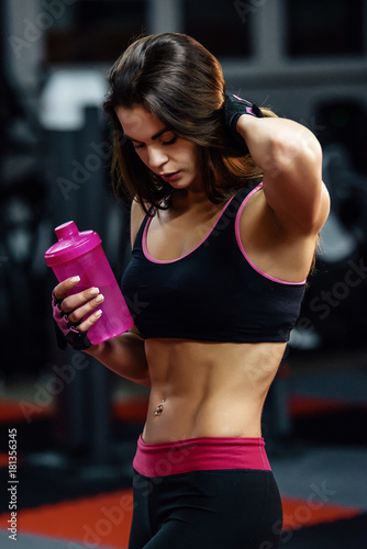 Athletic young woman after hard workout at gym. Fitness girl holds shaker with sportive nutrition.