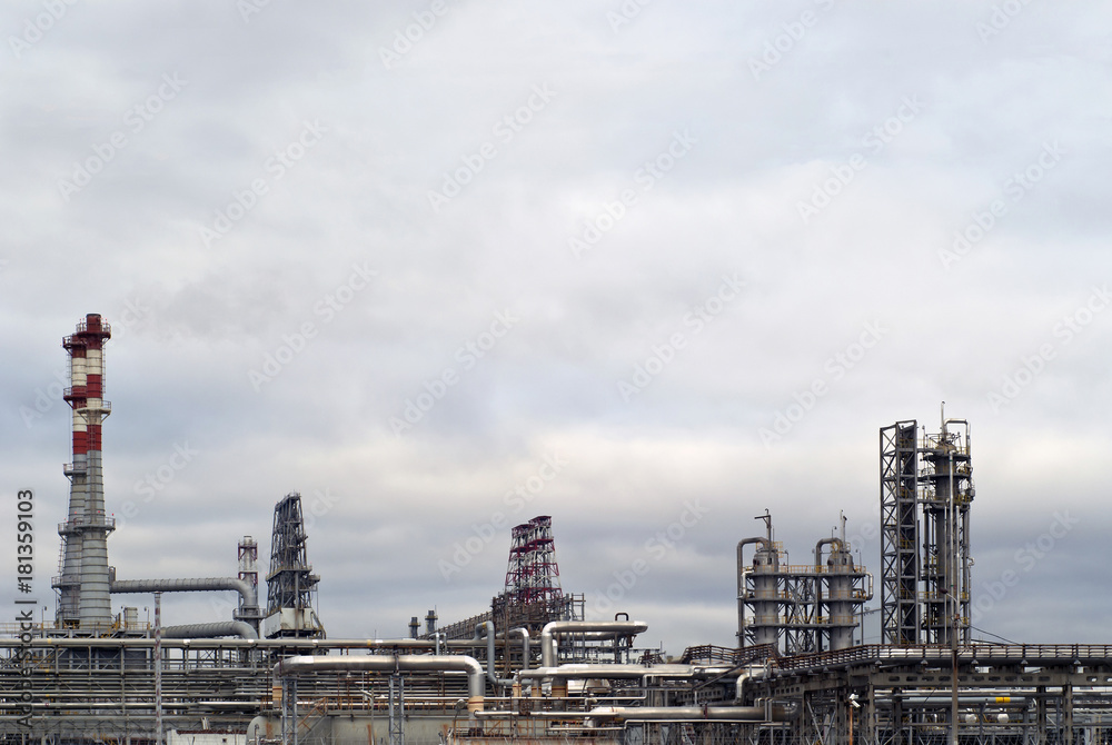 general view of a chemical or oil refinery with a multitude of pipelines, factory pipes and distillation columns under a cloudy sky