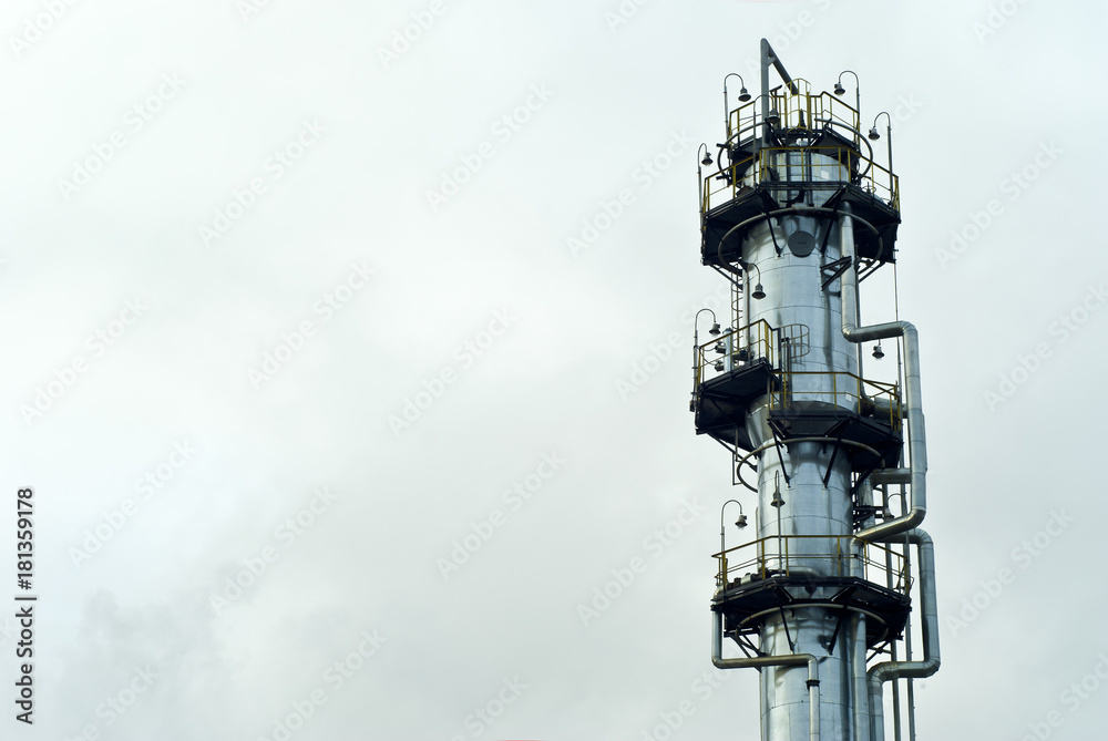 the upper part of a shiny gigantic metal fractionating column at a chemical or refinery with a sky background