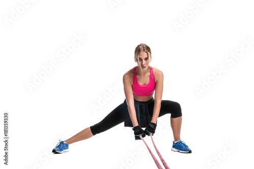 Fototapeta Naklejka Na Ścianę i Meble -  Strong woman using a resistance band in her exercise routine. Young woman performs fitness exercises on white background.