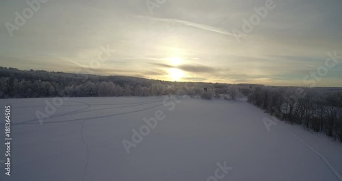A drone shot of a open feild surounded by trees and the sun is rising is the back