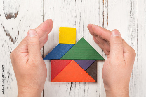 hands surround a wooden house made by tangram home insurance concept or representing home ownership