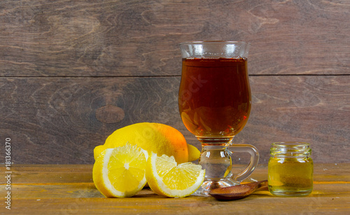 a cup of tea, lemon, lemon slices with a jar of honey and a wooden spoon on a wooden surface