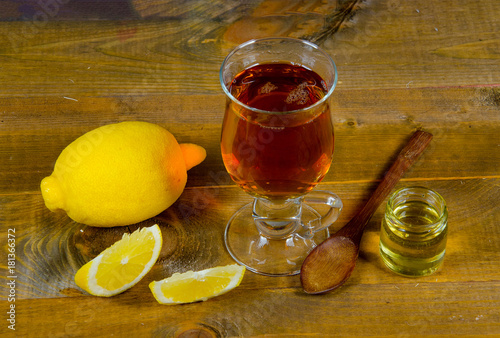 a cup of tea, lemon, lemon slices with a jar of honey and a wooden spoon on a wooden surface