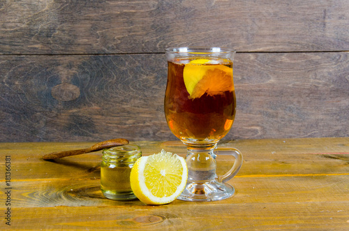 a cup of tea, lemon, lemon slices with a jar of honey and a wooden spoon on a wooden surface