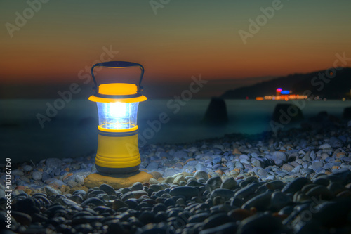 Luminous hand lantern standing on the pebble beach on the background of sea at dusk, Sochi, Russia
