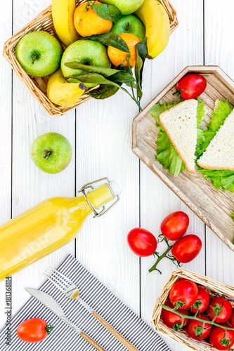 Healthy food for picnic. Sanwiches, fruits, vegetables, juice on tablecloth on white wooden background top view