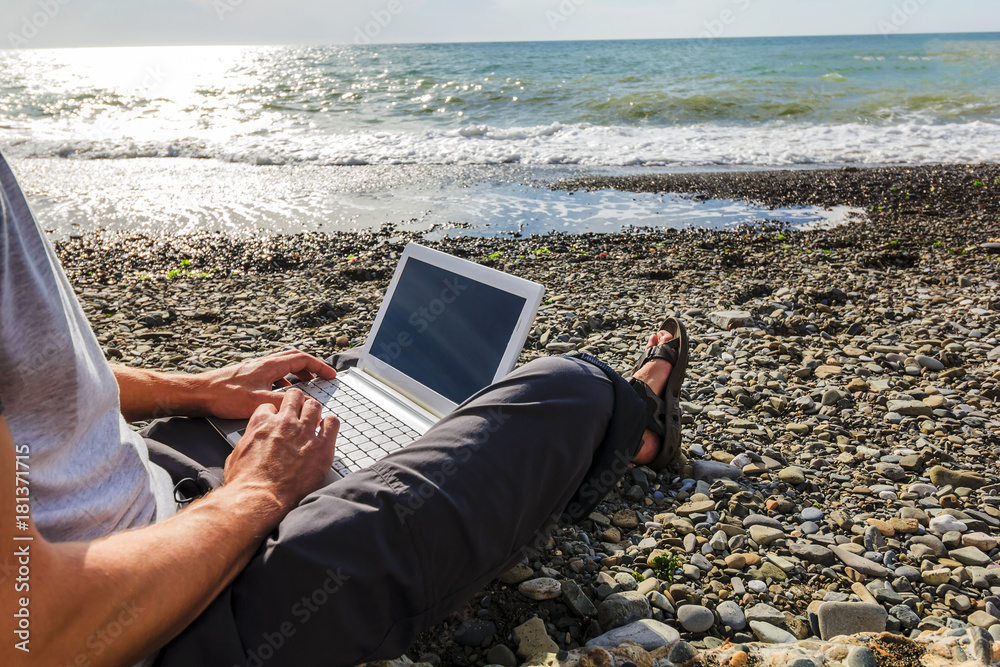 young man freelancer working with a laptop on the beach,close up screen