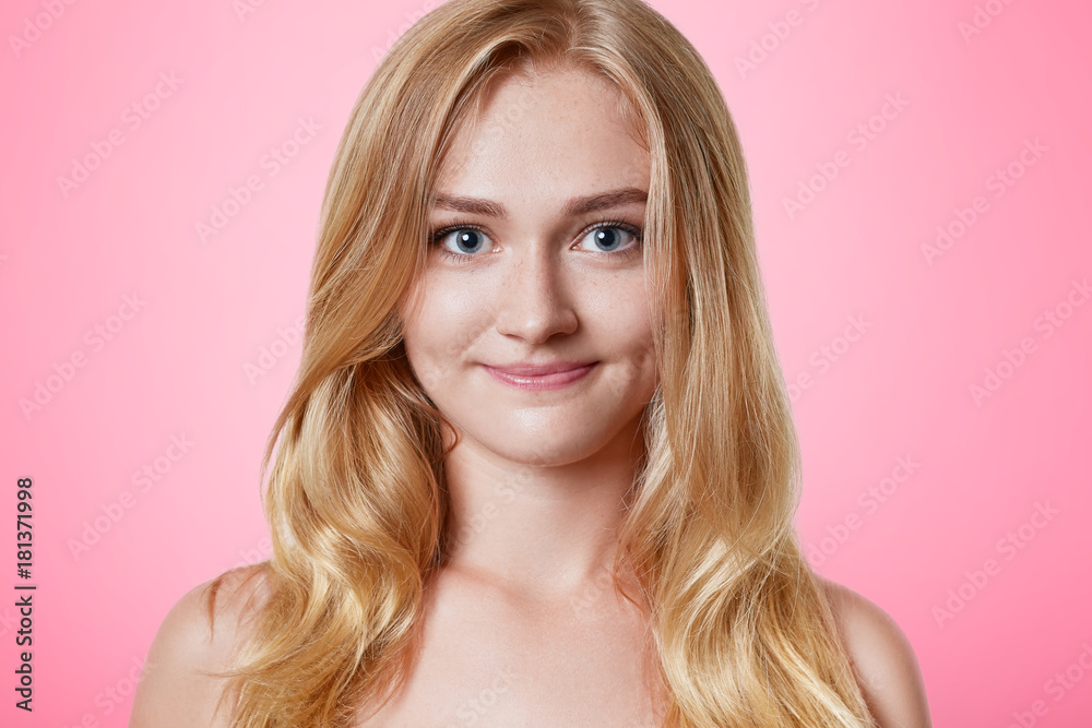 Pleasant looking female with pure healthy skin, warm appealing eyes and charming smile, has long light hair, looks directly into camera, isolated over pink background. Beauty and youth concept Pleasant looking female with pure healthy skin, warm appealing eyes and charming smile, has long light hair, looks directly into camera, isolated over pink background. Beauty and youth concept