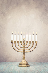 Bronze Hanukkah menorah with burning candles on wooden table front old vintage concrete wall background. Holiday greeting card concept. Retro style filtered photo