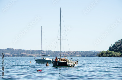 Two sailboats anchored in the lake. In the background campgrounds and hills with woods. © cromam70