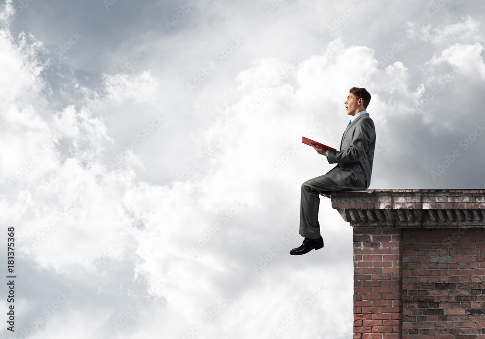 Man on roof edge reading book and cloudscape at background Man on roof edge reading book and cloudscape at background