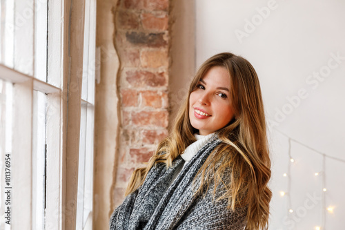 Фотография Cute woman is dreaming about christmas holidays in the white walls room with coz