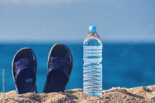 Bottles of pure water and pair of sandals on the beach sand against the sea.
