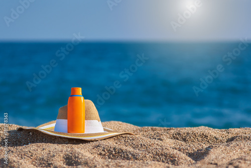 Bonnet hat and bottle of sunscreen against the sea.