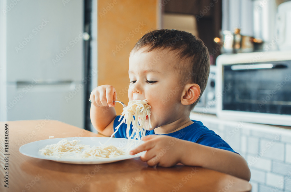Baby in the kitchen eagerly eating pasta Baby in the kitchen eagerly eating pasta