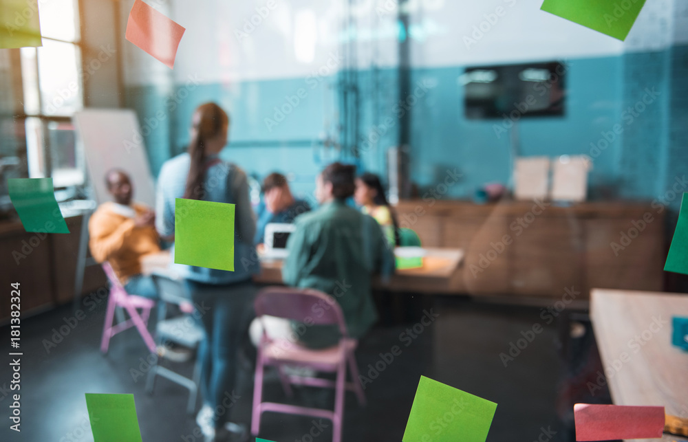 Young startup team having job together while situating at desk in modern office. Colourful post-it notes locating on window. New idea concept