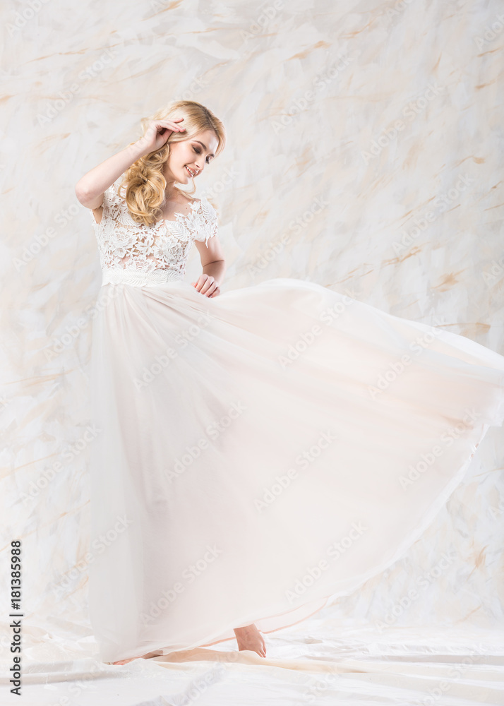 fashionable wedding dress, beautiful blonde, bride hairstyle and makeup concept - dance of young pretty woman in long luxury white gown indoors on light background, cute female model in a studio fashionable wedding dress, beautiful blonde, bride hairstyle and makeup concept - dance of young pretty woman in long luxury white gown indoors on light background, cute female model in a studio