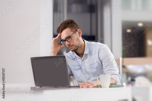 Pensive businessman reading something from laptop at office.