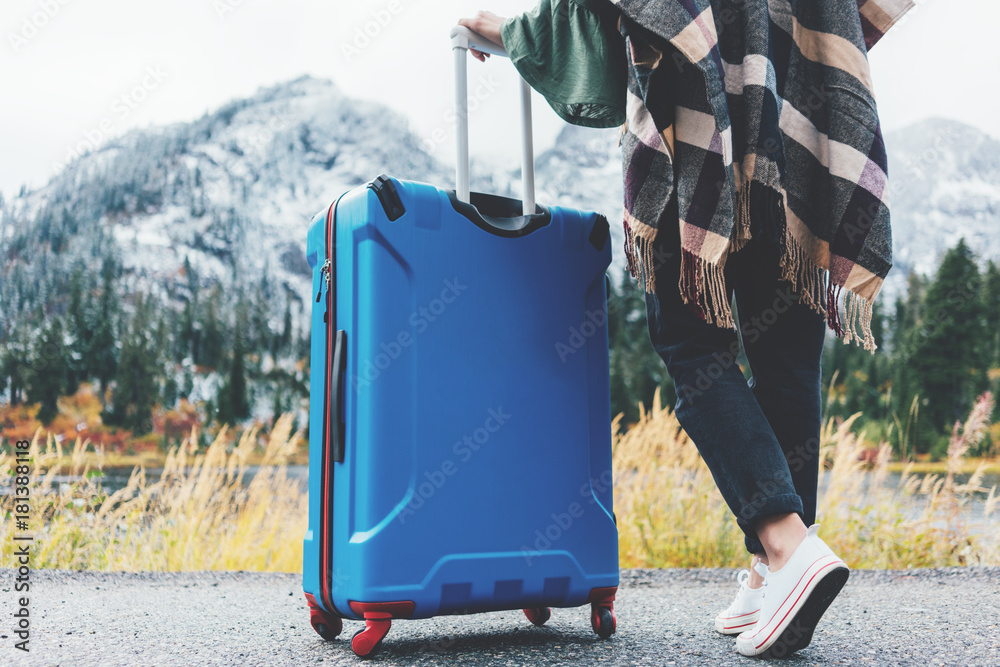 Φωτογραφία Traveling woman wearing poncho with bright blue suitcase standing next to stunning mountain wild