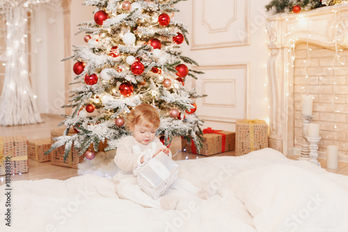 Family on Christmas . Baby girl opening Xmas presents. Children under Christmas tree with gift boxes and white fireplase. Decorated living room with christmas toys. Cozy warm winter day at home. photo