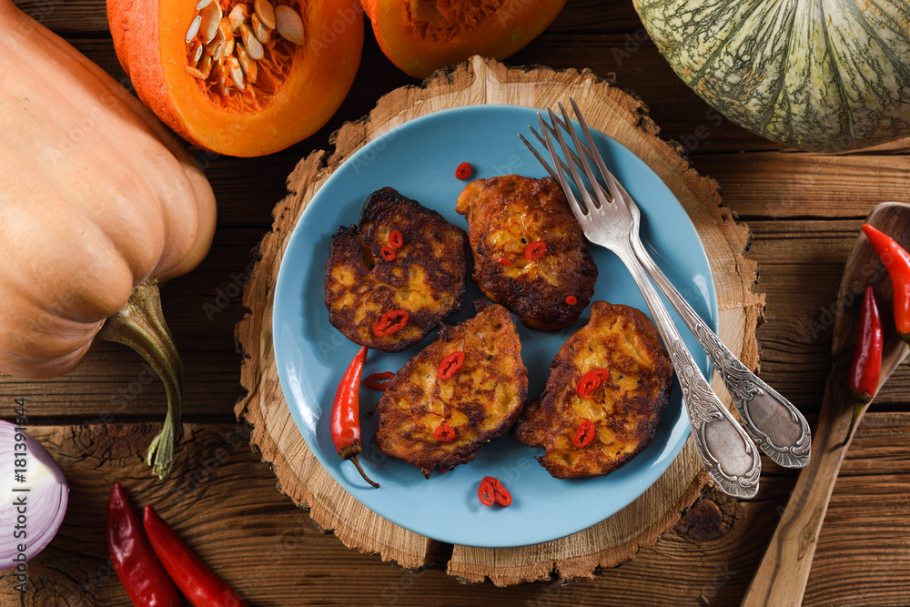 Healthy vegetarian dish flatlay. Pumpkin pancakes on wood slab decorated with chili peppers and raw pumpkins on rustic wooden background