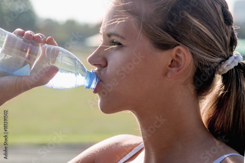 Young beautiful sports girl drinking water during morning jogging