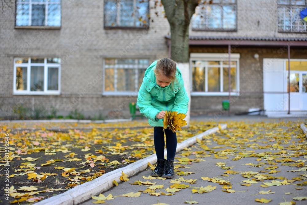 A girl in a green jacket collects yellow leaves in autumn