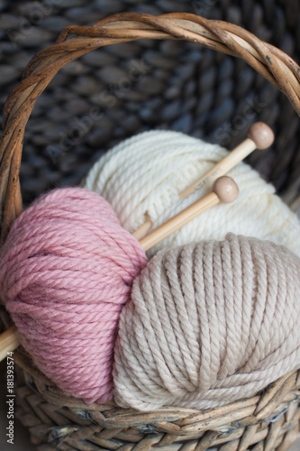 Yarn balls with knitting needles in the basket on the wooden background