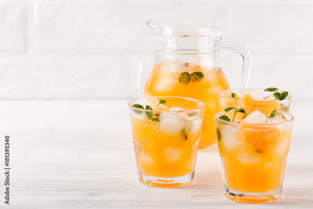 Mandarin cocktail with ice and mint in beautiful glasses and jug, fresh ripe citrus on white wooden background. Sweet orange juice. Close up photography. Selective focus Mandarin cocktail with ice and mint in beautiful glasses and jug, fresh ripe citrus on white wooden background. Sweet orange juice. Close up photography. Selective focus