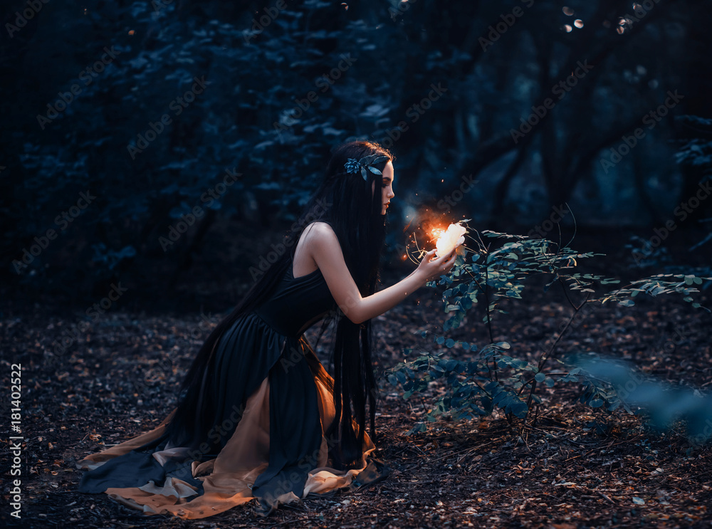 Obraz premium Bajeczna leśna nimfa z długimi włosami znalazła ognisty, ognisty kwiat, którym wylatują małe motyle i wróżki. Fotografia artystyczna